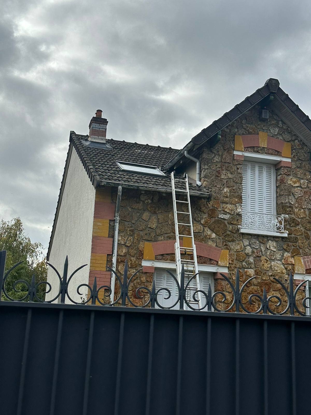 Maison avec façade à ravaler derrière une clôture.